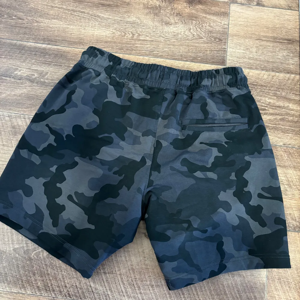 Better Bodies helt nya shorts. Shorts i kamouflage-mönster med en liten logotyp på vänster ben. Shortsen har en resår i midjan och en dragsko för att justera passformen. Det finns två fickor på sidorna och en ficka med dragkedja på baksidan.. Sportswear.