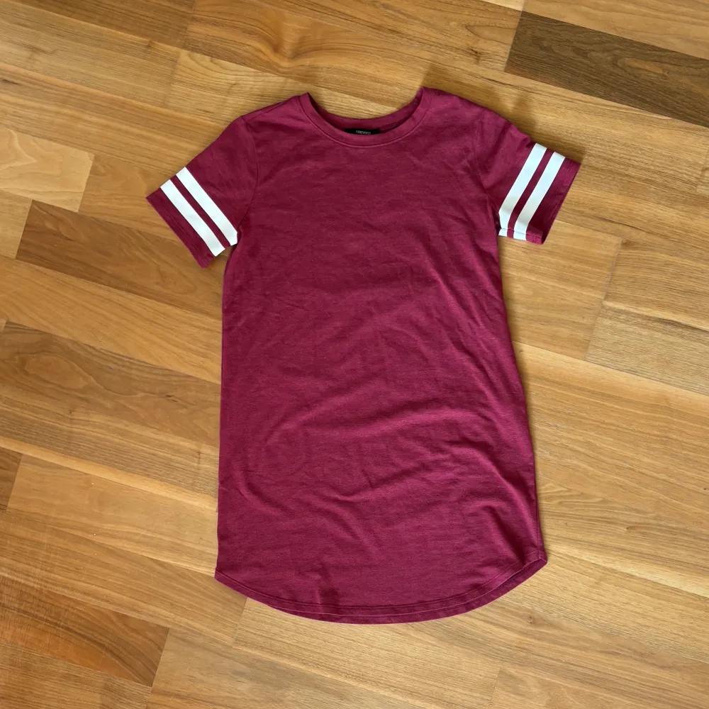 Lång, cool och stretchig t-shirt/ t-shirtklänninh med vita ”gummi”texturerade ränder på båda armarna från Forever 21. Storlek: S. Material: 57% bomull + 38% polyester + 5% elastan. :). T-shirts.