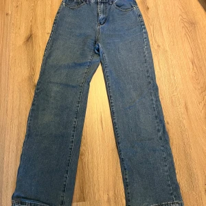 Blå jeansbyxor - Ett par blå jeansbyxor med raka ben och klassisk femficksdesign. Byxorna har en hög midja och är tillverkade i denim.💗