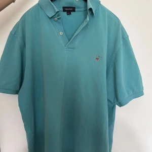 Turkos Gant pikétröja - Turkos gant pikétröja som är jätte stilig, man kan knäppa upp den vid kragen. Den är jätte snygg och har vita knappar.