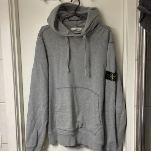 Stone island hoodie grå - En äkta stone island hoodie som jag köpte för två år sedan. Den har ett litet hål på ena armen (se på bild) och tre mindre slitningar på andra men inget som synd märkvärdigt.  Annars väldigt snygg. Strl L  Nypris 3500kr  Mitt pris 1200kr 