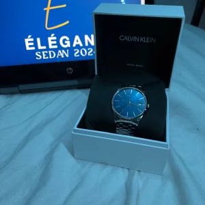 Calvin Klein Klocka - Med denna klocka tar du inte bara reda på tiden, du definierar den! Den blå urtavlan är en strålande detalj som omsluter varje ögonblick med elegant skönhet. För endast 449 är denna klockan din! Skick 9/10