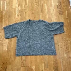 Grå stickad tröja - En grå stickad tröja med korta armar. Tröjan är använd cirka 3 gånger och inte använd på ett tag därför säljer jag den