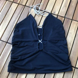 Svart korsettopp från BikBok - En svart korsettopp från BikBok i storlek M. Toppen har en djup urringning och smala axelband som knyts i nacken. Den är tillverkad av 95% polyester och 5% elastan, med foder av 100% polyester.