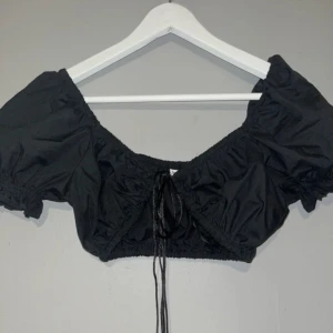 Liten topp med knyten i fram - Liten fest topp med snören i fram som man kan justera. Puffiga ärmar. Aldrig använd storlek M