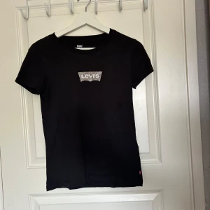 Svart t-shirt från Levi's - En svart t-shirt från Levi's med korta ärmar och en tryckt logotyp på bröstet. Använd några gånger i hemmet, säjer för att den är för liten!