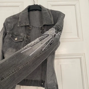 Jeansjacka med stenar - Grå jeansjacka med snygga stenar och glitter på ärmen!! Superfin & jättebra skick