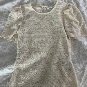 Beige spetsblus från Vila - En elegant beige spetsblus från Vila med korta puffärmar och rund halsringning. Blusen har ett detaljerat spetsmönster 💕 Ny utan prislapp 