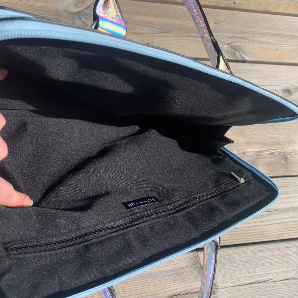Holographic laptop väska från Skinnydip med axelband, köpt ifrån London men aldrig använd.  Ficka på baksidan med magnetlås, ytterfack med 5 fickor. Stort fack för laptop och en innerficka.  CA; 34 cm lång, 27 cm hög, 5 cm bred (7 cm med ytterfacket). Väskor.