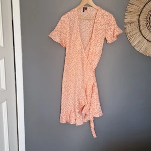 Sommarklänning omlott  - Snygg klänning använd ett fåtal gånger. Mönstrad i vitt och aprikos. Volangkant runt ärm och nertill. Nypris 500 kr