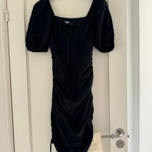 Svart kortärmad adoore klänning  - Adoore klänning, aldrig använd med prislapp kvar. Fel storlek tyvärr. Dragkedja på sidan. Resår också som gör att du själv kan reglera längden mellan att ha mini alt knälängd på ena sidan 🥹