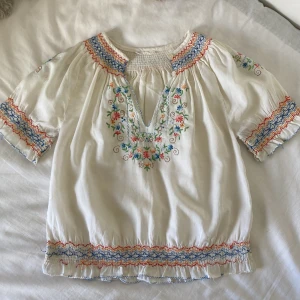Blus -  En så fin somrig blus med fina färgglada söm och insydda blommor 🌸 Perfekt nu till sommaren!💗 Den enda defekten är att vissa trådar är lite lösa längst ner, annars jättebra skick!⭐️