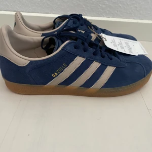 Nya retro Adidas Gazelle - storlek 38 - Adidas originals gazelle j i storlek 38. Färgen är marinblå och beige (night indigo/wonder taupe) Nya och oanvända med tags.  Populär färg med vintage inspiration.  Slutsålda.  Handball Spezial Samba