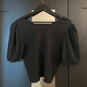 Svart topp med puffärm -  Jag säljer denna oanvända svarta topp från lager 157. Den är tunn luftig till sommaren och i mycket bra skick! 