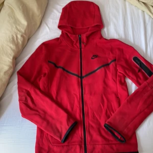 Nike tech röd - Säljer Nike tech som jag inte använder längre. Den är lite sliten och skicket är typ 6/10 och säljer den billigt för jag inte vill ha den längre, det är en liten skada vid kedjan som syns på bild 2.