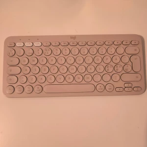Logitech K380 Bluetooth Tangentbord - Har 2 små "fläckar" visat i bild 3&4, de är små och man ser de inte under användning eftersom de är på baksidan eller under. Nypris 599kr. Kan koppla till dator, laptop, telefon och surfplatta. 124mm höjd 279mm bredd 16mm djup. 10m Bluetooth.