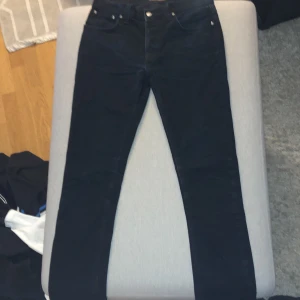 Svarta jeans från Nudie Jeans - Ett par svarta jeans från Nudie Jeans. Jeansen har en klassisk femficksdesign och är tillverkade i ett slitstarkt material. Jeansen är i nyskick och har aldrig använts. Säljs därför lite dyrare.