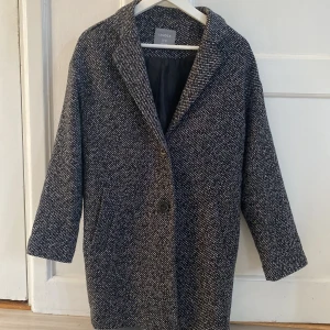 Grå-svart/vit kappa - Säljer denna fina vårkappa eftersom att den inte kommer till användning. Ett litet hål i sömnen på axeln - på bild tre. Nypris- 799kr