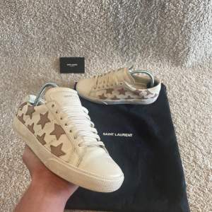 Säljer dessa Saint Laurent SL/01 Leather trainers i storleken 37. De är i färgen vit med snygga rosa stjärnor. De är i mycmet bra skick men lite använda, perfekta nu till våren/ sommaren! Vid minsta fråga är de bara att göra av sig!