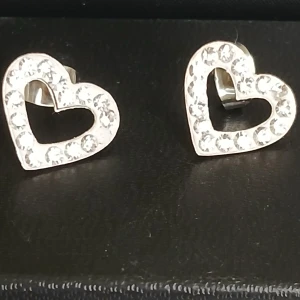 Örhängen - Hjärtformade örhängen. Med stenar. Använd endast ett fåtal gånger, det saknas en sten på ena örhänget vilket visas på sista bilde. Vid köp skickas det med 8 st extra örhängespluppar. 