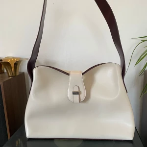 Vintage/retro väska från Fiorelli - Vintage/retro väska från Fiorelli i en modell som är supermodern nu! Vit/cremefärgad med burgundy accenter  Den har många år på nacken och därför några små defekter (ex. Lite färgad på baksidan mot kroppen och lite skrapad på axelbandet H:21cm L:31cm