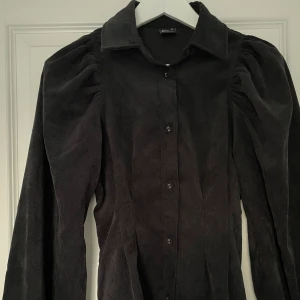 Manchester-liknande skjorta - Svart skjorta i manchester-liknande material från Gina Tricot. Storlek 32 men passar även större. Knappar framtill och i slutet av ärmarna, något figursydd. Fungerar även bra som overshirt. Så gott som nyskick!🎀 