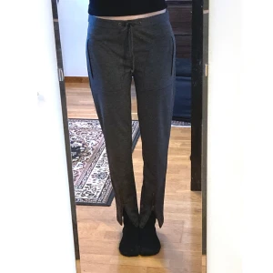 Mörkgrå mjukis slacks, S 36, low waist, straight leg, dragkedja, stilrena, tygbyxor - Kombination utav mjukisbyxor och slacks, mässingfärgade dragkedjor, knytband i midjan, två sidfickor, låg stretch. Mått i cm: midja 41; höft 45; benvidd nedanför grenen 26,5; benöppning 13,5; grenhöjd fram/bak 23,5/31; innerben 74.