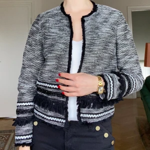 Tidlös tweedkavaj med fransar i svartvitt från H&M - Så snygg och femenin kavaj med fransar och andra dekorationer från H&M. Kavajen har lätta axelvaddar och ingen knäppning och ger en fin silhuett när den är på. Passar lika bra till jobbet som till vardags. Storlek 36. Går att tvätta i maskin på 30°c 