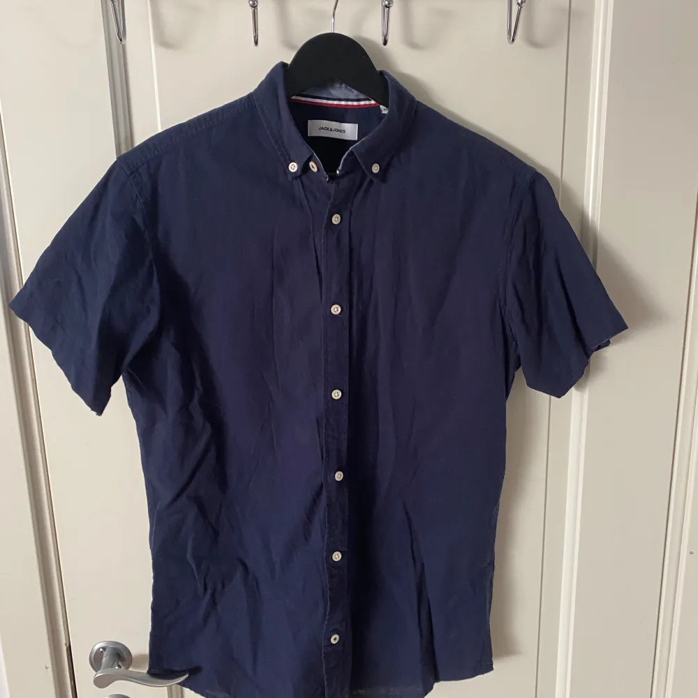 En Marinblå skjorta med korta ärmar från Jack & Jones i storleken xs. Den är använd 1-2 gånger så i super bra skick. Perfekt nu till sommaren.. Skjortor.