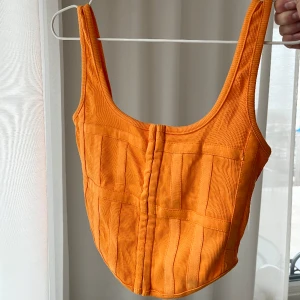 Orange topp - Korsettliknande topp i en snygg orange färg, prislapp kvar! Passar någon med mindre byst. Strl L men mer som S/M. 