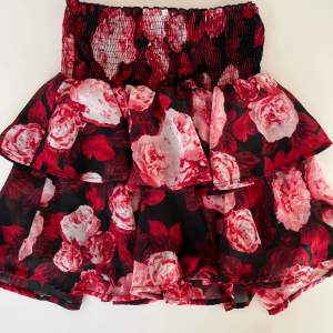 Röd/vit/svart kort kjol med volang i flera lager. Stretchig smock i midjan.   NA-KD Storlek XS, passar även S pga stretchig. 100% polyester