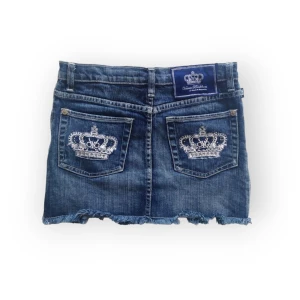 Victoria Beckham jeans kjol - Mörk jeanskjol med silverkronor och rhinestones på bakfickorna. Storlek W29, passar mig som brukar ha 34. Midja: 37 cm, längd: 32 cm. Inga defekter förutom att vissa stenar fallit av, syns på bilden. Fråga gärna om fler bilder 💕