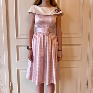 Rosa rutig klänning, Emmy Design - Jätteskön rosa rutig klänning. Vit krage med jordgubbar. Storlek 38. Brett skärp. Modellen på bilden är 173 cm och har storlek 38 i de flesta andra kläder. Aldrig använd. Vi har lagt ner vår klänningsbutik och säljer ut. Ny pris är 2000-3000kr