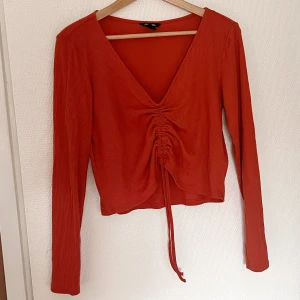 Ribbad topp - Långärmad ribbad topp med snörning framtil som gör att längden kan justeras 🌻 Ljusröd färg från Monki. Stl L.