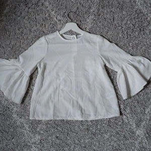 Vit blus - Superfin vit blus med volang trekvartsärmar och flowy tyg. Har storlek 134 men sitter som en xs, kan skicka mer bilder kring passform om önskas. Liten fläck på framsidan men det syns inte vid användning.