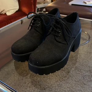 Svarta skor med klack och snörning - Ett par svarta platåpumps med snörning och hög klack. Vagabond. Skorna har en robust sula och är tillverkade i ett syntetmaterial. mullrigt använda och i fint skick. Nypris 1000kr. Frakt ingår ej.