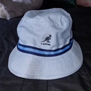 En ljusblå hatt från Kangol med blå ränder runtom. Hatten har en avslappnad passform och är lämplig för olika säsonger. storlek s, väldigt fin.. knappt använd. 