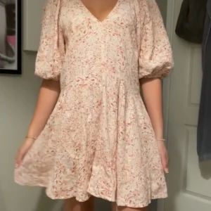 Blommig kortklänning - En vacker blommig kortklänning med puffärmar och v-ringad hals. Klänningen har en lös passform och är perfekt för sommarens festligheter.