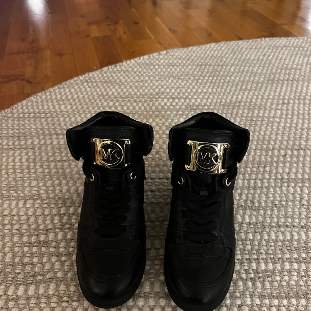 Svarta Michael kors sneakers med kilklack. Guldig logga. Väldigt bra skick, knappt använda. Storlek 38. Kan skickas om köpare betalar frakt.  Säljs för 400kr. Skor.