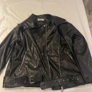 Skinn jacka  - Stor baggy skinnjacka med knappar, dragkedja och ett bälte vid midjan. Väldigt mycket rockstil 