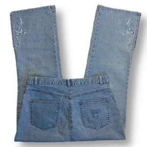 Ankeljeans  - Jättefina korta ankel jeans med fjäril på baken och blommor längst ner vi anklarna. Finns slits, syns på sista bilden. MÅTT: Midjebredd 40/41cm, höftbredd 49cm & innerbenslängd 65cm 