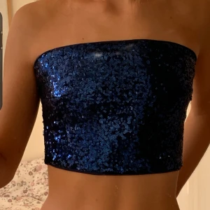 Festtopp  - Bandeau topp med glittriga, blå paljetter från NA-KD i storlek 34. Perfekt festtopp!! Endast använd en gång och det är därför jag säljer den. På insidan har den sockerplast som håller toppen på plats så den inte åker ner!!