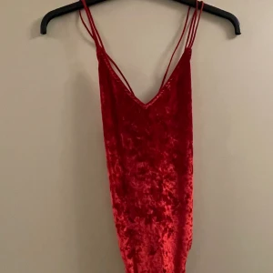 Velour body - Röd velour body från H&M, köpt några år tillbaka. Urringad framme och banden korsar sig över ryggen. Använd 1 gång, toppskick! 