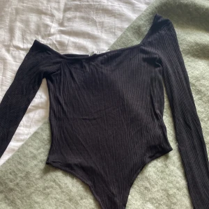 Asymmetrisk body - Svart body med långa ärmar. Den är asymmetrisk i modellen. Den är ribbad.