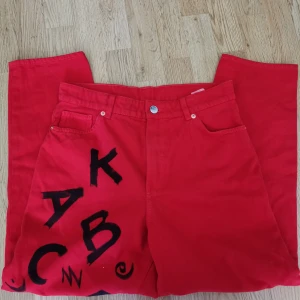 Röda jeans byxor med svart tryck - Röda jeans med bokstäver som detaljer. Storlek 30, väldigt fint skick (enbart provade av mig och nästan oanvända innan det). Lösare passform på mig.  Hämtning, annars betalas frakt av köparen. Bara att skriva vid frågor eller bud! 🌻 