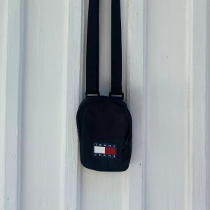 Axelremsväska - Tommy Jeans - Knappt använd svart axelremsväska från Tommy Jeans, perfekt att medbringa till stranden eller stan 🤍❤️ Remmens längd går att justera, och är som längst 145 cm lång 📏 Väskans dimension är 11x17x3 cm 🧳 Nypris: 459 kr.