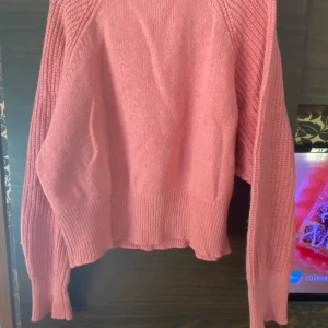 Stickad tröja - En rosa stickad tröja. Det är ett litet svart streck nere vid mudden på tröjan.