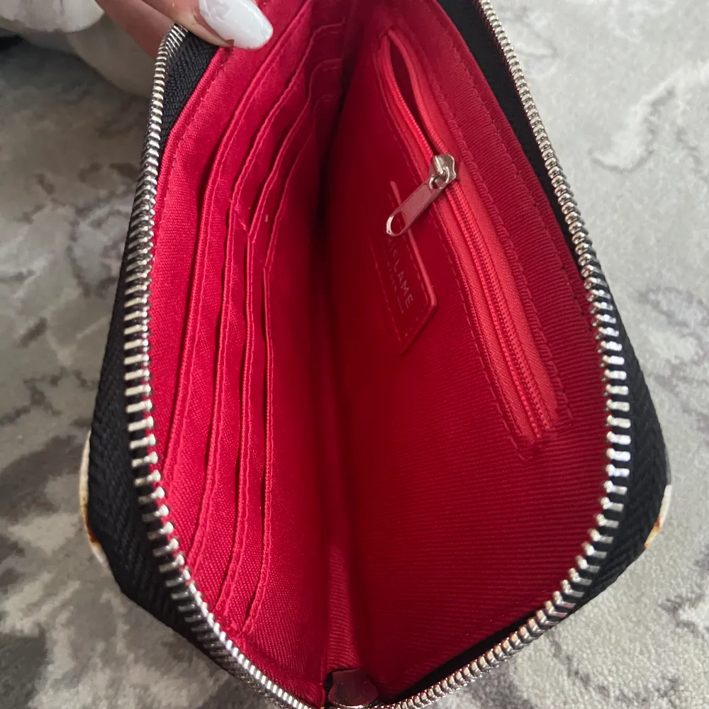 Plånbok med zebra mönster röd i insidan med en svart fluffboll som hänger på utsidan som dekoration . Accessoarer.