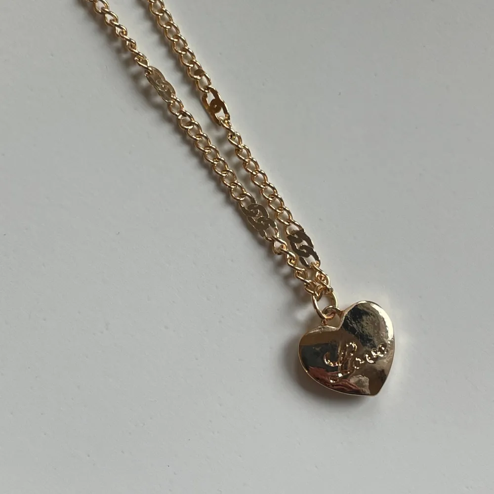 Halsband i rostfritt stål med guldplätering, ett hjärta där det står love, aldrig använt . Accessoarer.