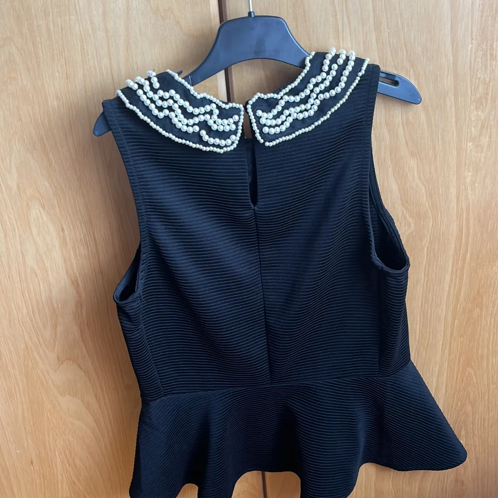 Aldrig använd topp med pärlbroderier på kragen, peplum formad. Lätt stretchig tyg. Yläosat.